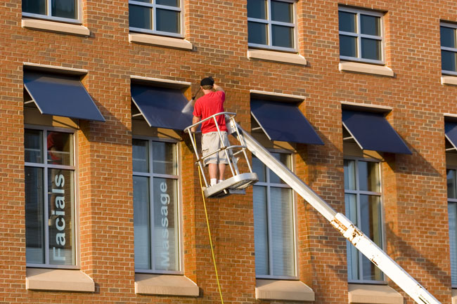 Worker on a crane pressure washing a building facade