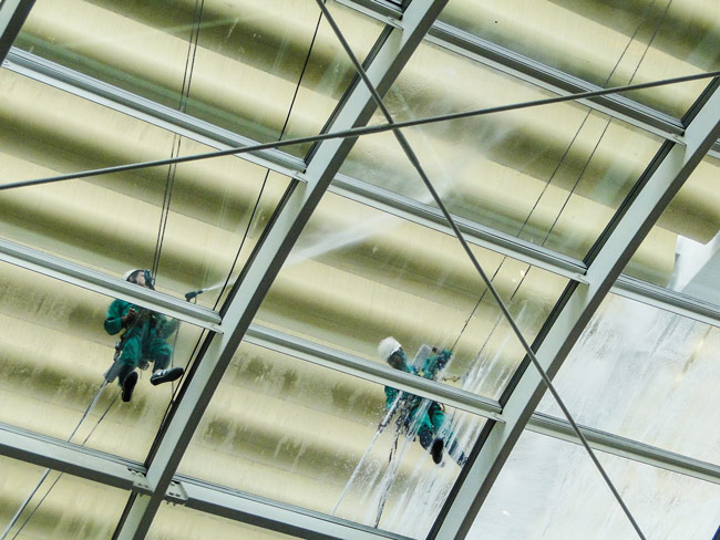 Two workers with pressure and steam machines cleaning a glass roof top