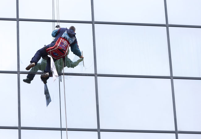 Worker washing building windows with harness